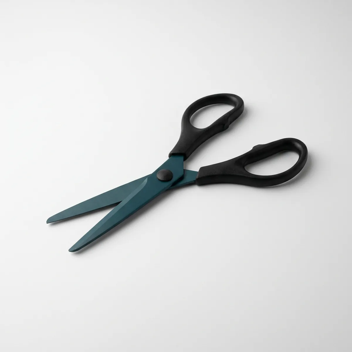 Pair of stainless steel tape scissors with dark teal coated blades, rounded tips and matte black handles, lying diagonally with blades slightly open